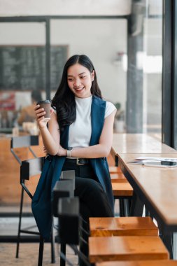 Gülümseyen kadın şık bir kafede kahve fincanı tutuyor, modern iç tasarım ve doğal ışıklandırma sergiliyor..