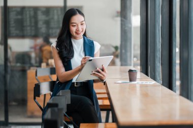 Modern iş kültürü ve teknolojisinin sergilendiği şık bir kafede tablet kullanan iş kadını..