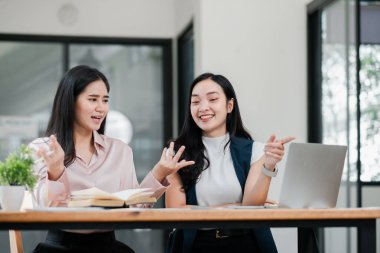 Modern ofis ortamında iki kadın, bir dizüstü bilgisayar ve masadaki belgeleri tartışıyorlar..