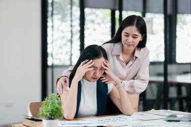 İlgili bir iş arkadaşı, stresli bir iş kadınını masasında, parlak ve modern bir ofis ortamında teselli eder..