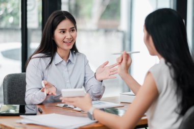 Modern ofis ortamında iş stratejilerini tartışan iki kadın, takım çalışması ve profesyonel işbirliği sergiliyor..