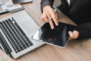 İşadamı, ahşap bir masada dijital tablet ve laptop kullanarak modern teknolojiyi profesyonel bir ortamda sergiliyor..