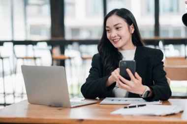 Akıllı telefon ve dizüstü bilgisayarla modern ofis ortamında birden fazla iş yapan kendine güvenen bir iş kadını..