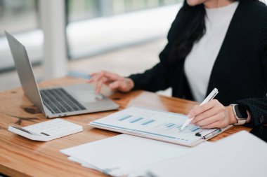 Profesyonel bir kadın dizüstü bilgisayardaki çizelge ve grafikleri inceliyor ve ahşap bir masada, finansal analize odaklanıyor..