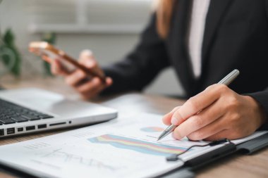 Finansal tabloları inceleyen, akıllı telefon kullanan, modern ofis çalışmalarını sergileyen bir iş adamının yakın plan çekimi..