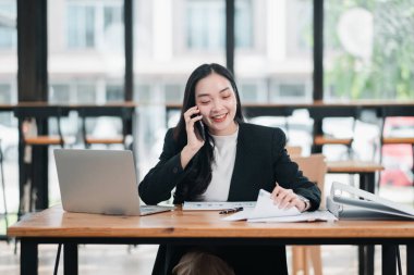 Parlak, modern ofis ortamında telefon ve evrak işleriyle uğraşan profesyonel bir kadın..