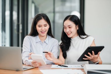 Çağdaş bir ofis ortamında dijital cihazlar kullanarak ve belgeleri tartışarak birlikte çalışan iki kadın..