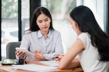 İki kadın bir iş görüşmesinde. Parlak ve modern ofis ortamında belgeleri gözden geçiriyorlar..
