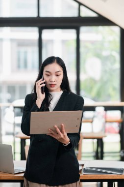Parlak, modern ofis ortamında, tablet ve telefonla birden fazla iş yapan profesyonel bir kadın..