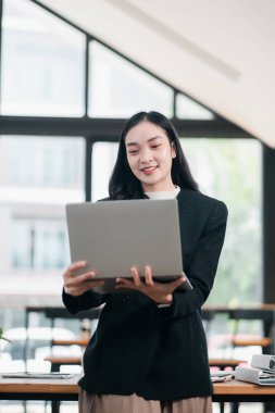 Modern ofis ortamında profesyonel bir kadın dizüstü bilgisayar tutuyor, güven ve teknoloji gösteriyor..