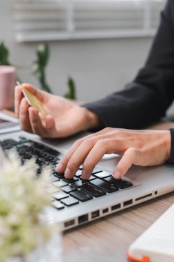 Eller, elinde bir kredi kartı tutarken dizüstü bilgisayarın klavyesinde yazarken, modern bir çalışma alanında online alışveriş ve e-ticareti sembolize ediyor..