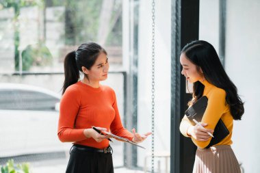 Modern ofis ortamında iki kadın, profesyonel etkileşim ve işbirliğini vurgulayarak, odaklanmış bir konuşma yapıyorlar..