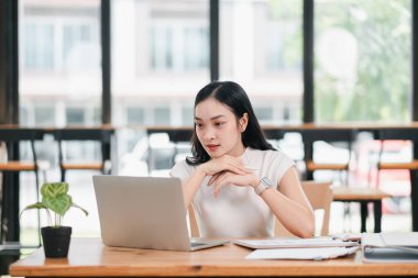 Minimalist dekor ve doğal ışık ile çevrili, parlak, modern ofis ortamında dizüstü bilgisayar kullanan odaklı bir kadın..