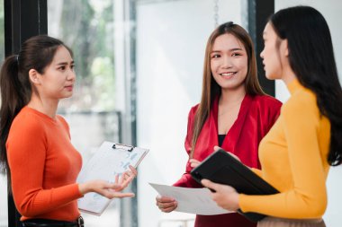 Üç kadın, parlak ve modern bir ofis ortamında fikir ve belgeleri paylaşıyorlar..