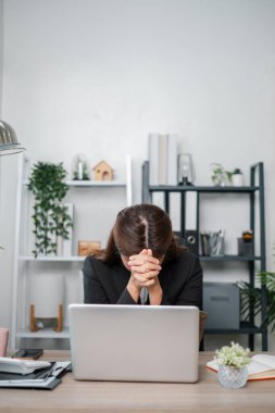 İş kadını kendini masasında stresli hissediyor, modern bir ofiste bitki ve raflarla birlikte dizüstü bilgisayarla çalışıyor..