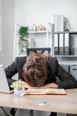 Yorgun iş kadını ofis ortamında başını bir masaya yaslayıp stresi ve tükenmeyi sembolize ediyor..