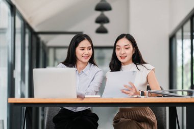 Modern ofis ortamında laptoplar ve belgelerle birlikte çalışan iki kadın takım çalışması ve işbirliği sergiliyor..