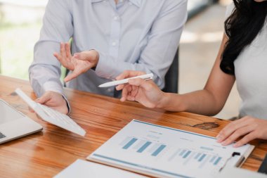 Çağdaş bir ofis ortamında yapılan bir iş toplantısında finansal tablolar ve verileri analiz eden iki profesyonel.