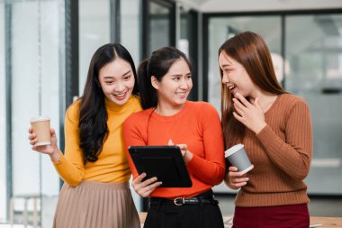 Modern ofis ortamında üç kadın, kahveyi paylaşıyorlar ve tablet kullanıyorlar, takım çalışması ve arkadaşlık sergiliyorlar..