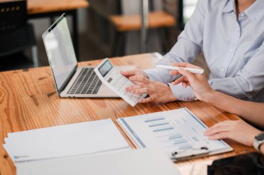 Meslektaşlar, ahşap ofis masasında dizüstü bilgisayar ve hesap makinesi kullanarak finansal analizde işbirliği yaparlar..