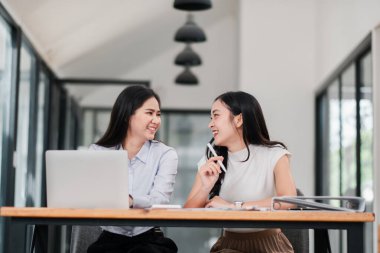 Modern ofis ortamında gülümseyen ve konuşan iki kadın takım çalışması ve işbirliği sergiliyor..