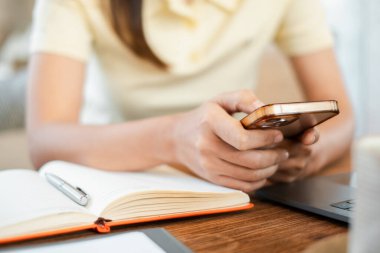 Ahşap bir masanın üzerinde elinde dizüstü bilgisayarla akıllı telefon tutan bir kadının samimi bir çalışma ortamı oluşturduğu yakın plan..