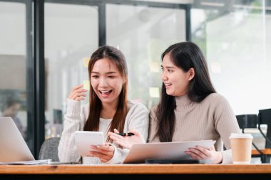 Modern ofis ortamında dizüstü bilgisayarlar ve tabletler kullanarak canlı bir tartışmaya giren iki genç kadın..