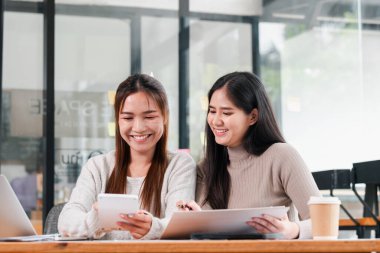 Modern bir ofiste birlikte çalışan iki kadın, teknolojiyi kullanıyor ve fikirleri paylaşıyor, takım çalışması ve işbirliği sergiliyor..