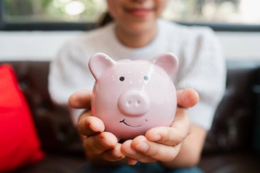 Pembe domuz kumbarası tutan bir kadının yakın plan çekimi. Tasarruf, finans ve bütçeyi rahat bir ortamda temsil ediyor..