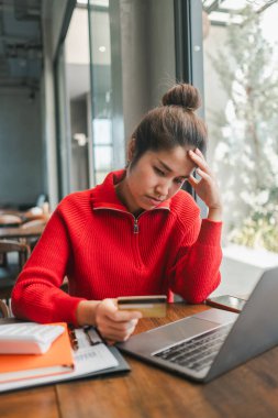 Kırmızı kazaklı, şık bir kafede online alışveriş için dizüstü bilgisayar ve kredi kartı kullanan odaklanmış bir kadın..