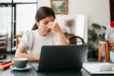 Kahve ve bitkilerle dolu rahat bir ofiste dizüstü bilgisayarla çalışan bir kadın stresli görünüyor..