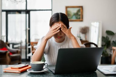 Masada oturan bir kadın, rahat bir oturma odasında elinde bir fincan kahveyle dizüstü bilgisayarla çalışırken strese girdi..
