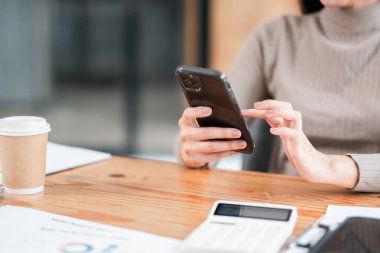 Ofis masasında kahve ve hesap makinesiyle akıllı telefon kullanan profesyonel bir kadın üretkenlik ve teknolojiye odaklanıyor..