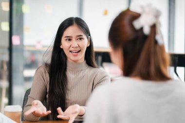 Modern ofis ortamında iş arkadaşıyla sohbet eden gülümseyen genç bir kadın..