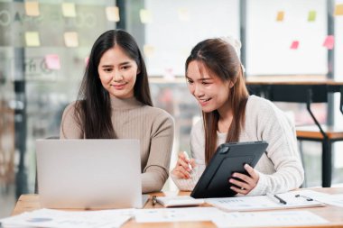 Modern bir ofiste birlikte çalışan iki genç kadın yaratıcı bir proje için dizüstü bilgisayar ve tablet kullanıyorlar..