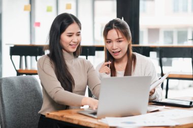 Parlak, modern bir ofiste dizüstü bilgisayarda çalışan iki kadın fikirleri tartışıyor ve belgeleri paylaşıyorlar..