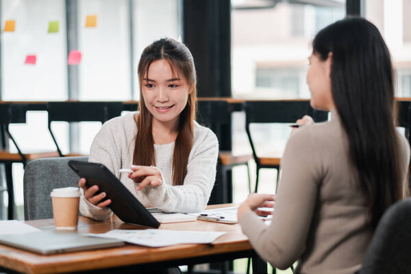 Две женщины обсуждают работу в современном офисе, пользуются планшетом и кофе. Идеально подходит для бизнеса и командной работы.