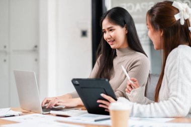 Modern bir ofiste birlikte çalışan iki kadın, dizüstü bilgisayar ve tablet kullanıyorlar, fikirleri tartışıyor ve bir proje üzerinde işbirliği yapıyorlar..