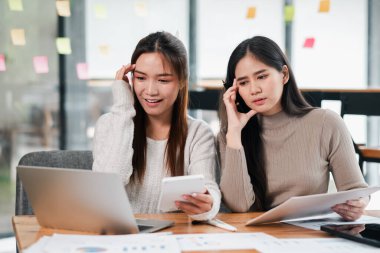 Modern bir ofiste birlikte çalışan iki genç kadın, bir proje için dizüstü bilgisayar ve belgeler kullanıyorlar..