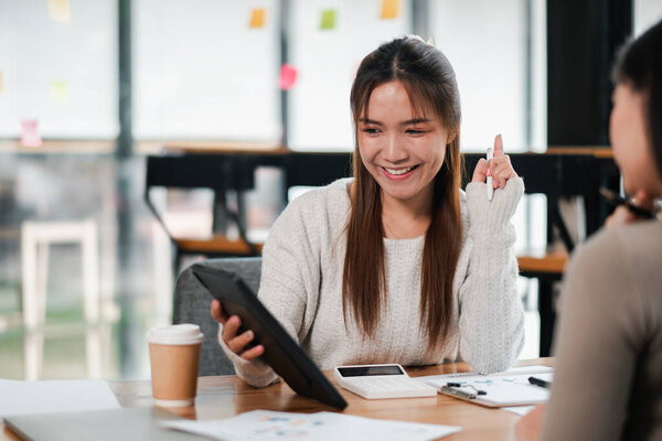 Веселая молодая женщина с планшетом в современной офисной среде, в окружении коллег и кофе.