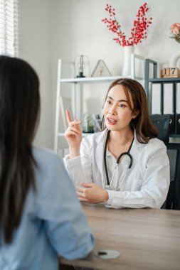 Beyaz önlüklü kadın doktor, modern bir muayenehane ortamında hastasıyla tartışıyor..