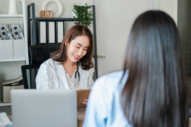 Modern bir muayenehanede bir hastaya danışılırken gülümseyen kadın doktor, sağlık ve sağlık hizmetlerini vurguladı.
