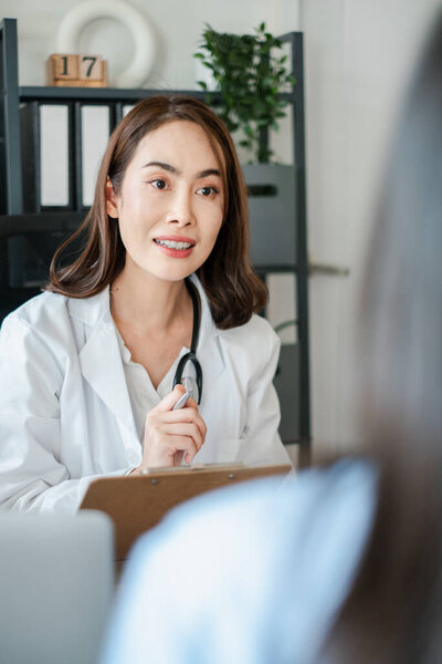 Female doctor in a white coat consulting a patient, holding a clipboard in a modern clinic setting.