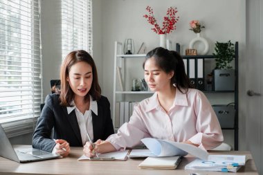 İki iş kadını bir masada birlikte çalışıyor. Parlak ve modern ofis ortamında belgeleri gözden geçiriyorlar..