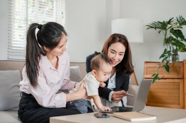 İki kadın ve bir bebek, parlak, modern bir oturma odasında dizüstü bilgisayarla etkileşime geçerek aile bağlarını ve teknolojilerini sergiliyorlar..