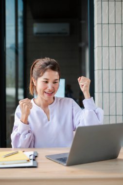 Bir dizüstü bilgisayar kullanırken heyecanını ifade eden neşeli bir kadın profesyonel bir ortamda başarı ve başarıyı simgeliyor..