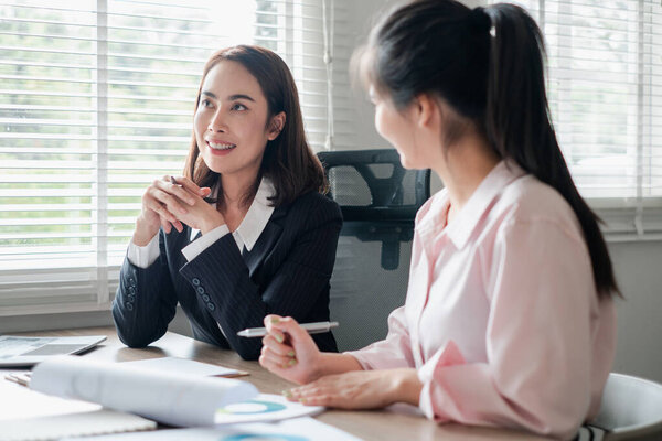 Two women engaged in a business meeting, discussing documents in a bright office environment.