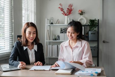 Modern ofis ortamında dokümanları doğal ışık altında tartışan iki kadın iş görüşmesindeler..