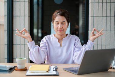 Genç bir kadın masasında meditasyon yapıyor, modern ofis ortamında rahatlama ve farkındalığı teşvik ediyor..