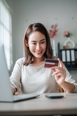 Bilgisayarla alışveriş yaparken elinde kredi kartı tutan bir kadın modern e-ticaret ve güvenli online işlemler sergiliyor..